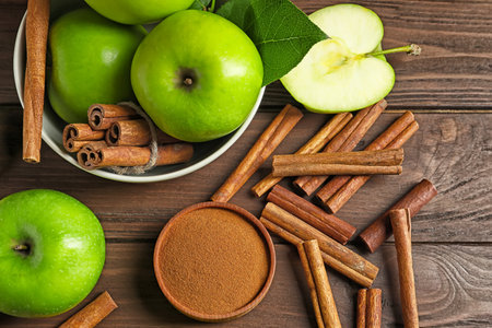 Fresh apples with cinnamon sticks and powder on wooden table, top viewの写真素材