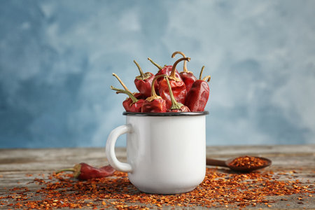 Mug with dry chili peppers and powder on wooden table