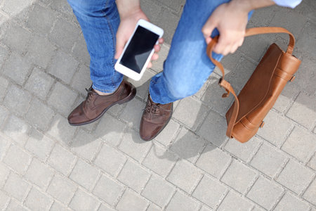 Man in stylish leather shoes using mobile phone outdoors, closeupの写真素材