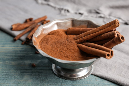 Bowl with aromatic cinnamon powder and sticks on wooden backgroundの写真素材