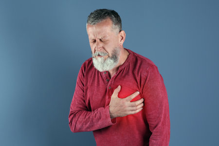 Mature man having heart attack on color background