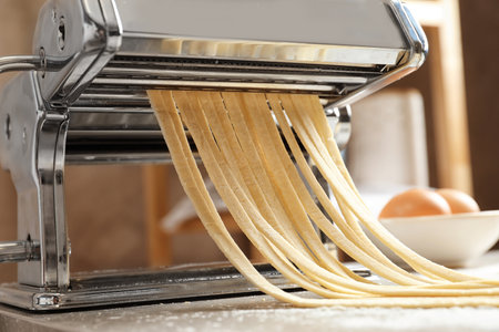 Pasta maker with dough on kitchen tableの写真素材