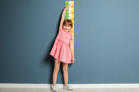 Little girl measuring her height near color wallの写真素材