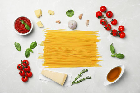 Beautiful composition with raw pasta and ingredients for sauce on table, top viewの写真素材
