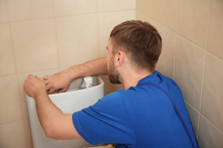 Professional plumber in uniform fixing toilet tank indoorsの写真素材