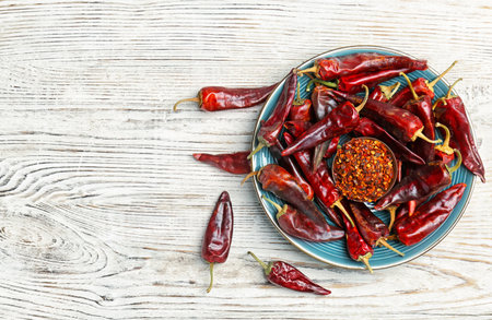 Plate with dry chili peppers and powder on wooden backgroundの写真素材