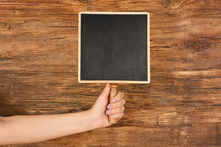 Woman holding small chalkboard on wooden backgroundの写真素材