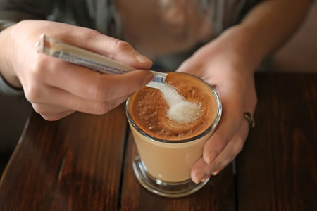Woman adding sugar to aromatic coffee at wooden tableの写真素材