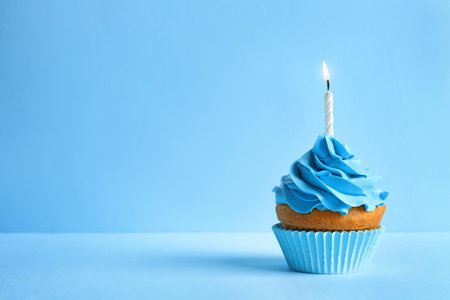Delicious birthday cupcake with candle on color backgroundの写真素材