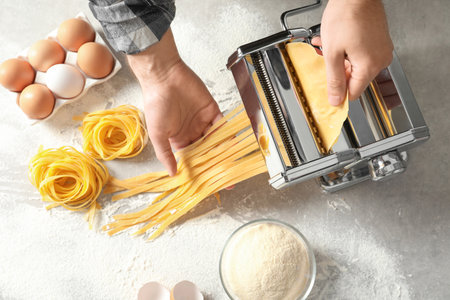 Young man preparing noodles with pasta maker at table, top viewの写真素材