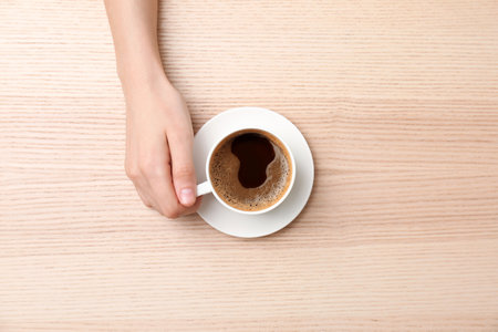 Young woman with cup of delicious hot coffee on wooden background, top view
