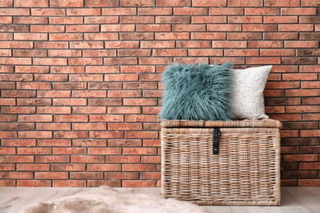 Soft pillows on wicker chest near brick wallの写真素材