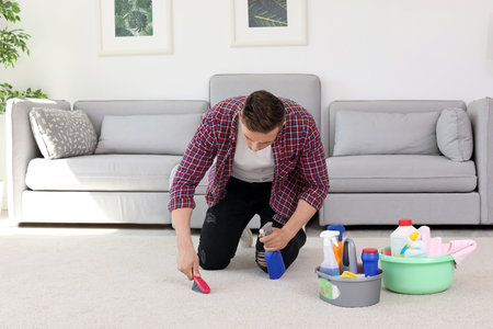 Young man cleaning carpet with brush at homeの写真素材