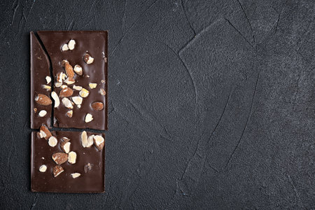 Delicious chocolate bar with nuts on dark table, top view