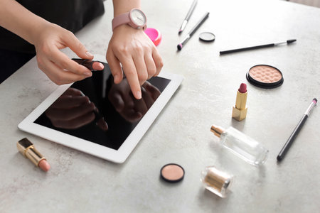 Young woman with makeup products using tablet at table. beauty blogger