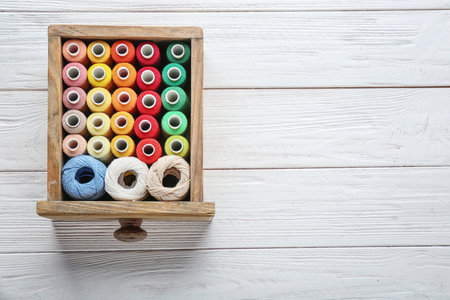 Drawer with colorful sewing threads on wooden background, top viewの写真素材
