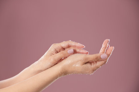 Young woman applying natural scrub on hands against color backgroundの写真素材