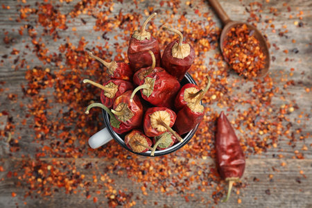 Mug with dry chili peppers and powder on wooden backgroundの写真素材