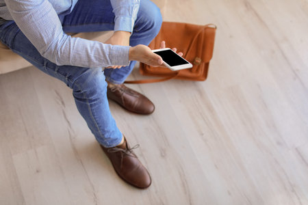 Man in elegant shoes using mobile phone indoorsの写真素材