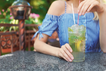 Young woman with glass of tasty lemonade at table in cafe, outdoors. natural detox drinkの写真素材