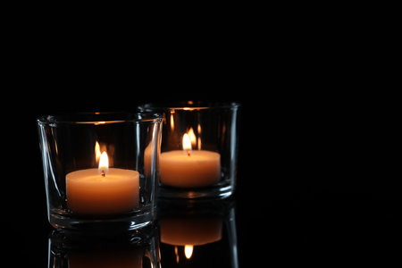 Wax candles in glasses burning on dark backgroundの写真素材