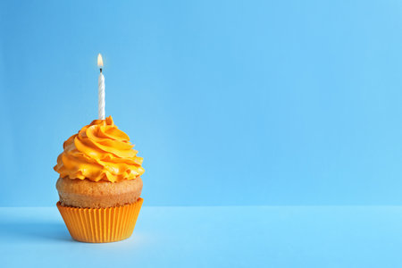 Delicious birthday cupcake with candle on color backgroundの写真素材