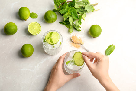 Young woman making delicious mint julep cocktail at table