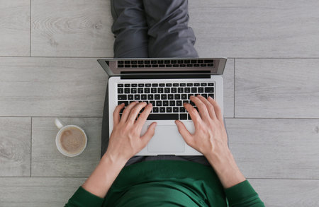 Young man using laptop while sitting on floor, top viewの写真素材
