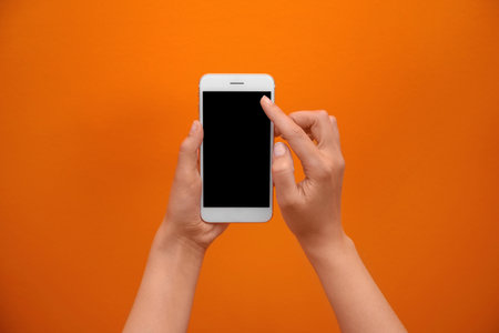 Young woman holding mobile phone with blank screen in hand on color backgroundの写真素材