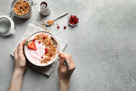 Woman eating tasty yogurt with berries and granola at table, top viewの写真素材