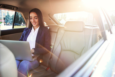 Young businesswoman with laptop in carの写真素材