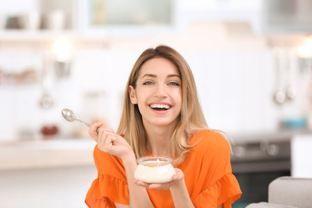 Young attractive woman eating tasty yogurt in the kitchenの写真素材