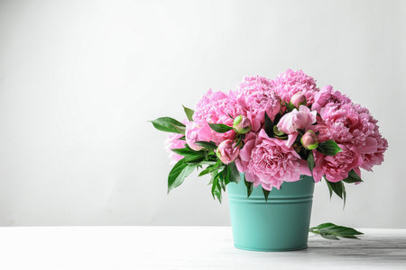 Bucket with beautiful peony flowers on table against light backgroundの写真素材