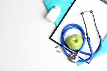 Flat lay composition with stethoscope, apple and clipboard on light background. medical equipmentの写真素材