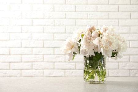 Vase with beautiful blooming peonies on table near brick wallの写真素材