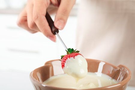 Woman dipping ripe strawberry into bowl with white chocolate fondue, closeupの写真素材