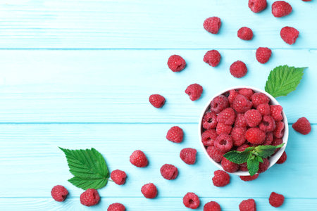Bowl with ripe aromatic raspberries on wooden table, top view