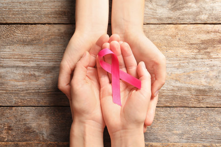 Women holding pink ribbon on wooden background, top view. cancer awarenessの写真素材