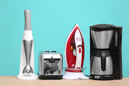 Household and kitchen appliances on table against color background. Interior element
