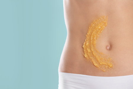 Young woman with natural scrub on her belly against color background, closeupの写真素材