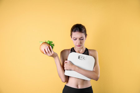 Young beautiful woman with scales and sandwich on color background. weight loss motivationの写真素材