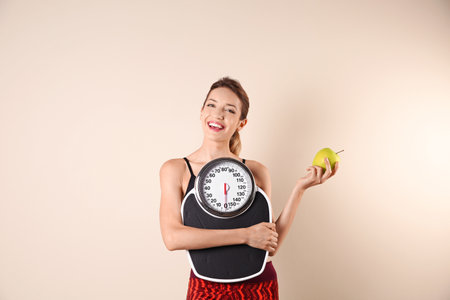 Young beautiful woman with scales and apple on light background. weight loss motivationの写真素材