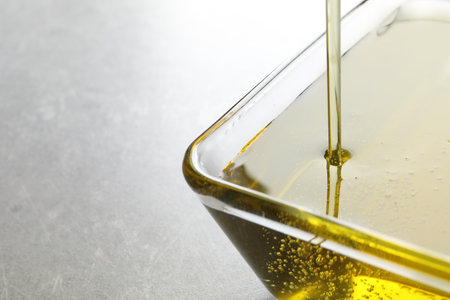 Pouring fresh olive oil into bowl on gray background, closeupの写真素材