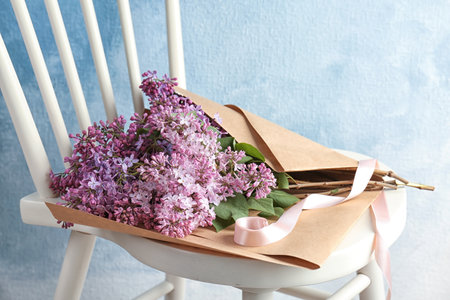 Beautiful blossoming lilac on chair against color background. spring flowersの写真素材