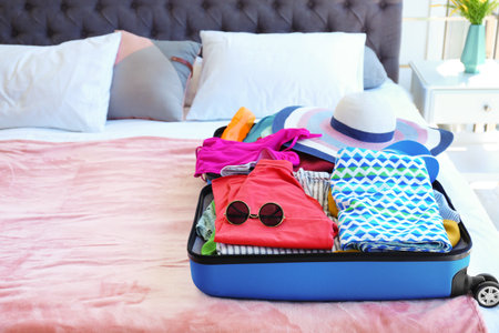 Open suitcase with beach clothes and accessories on bed indoorsの写真素材