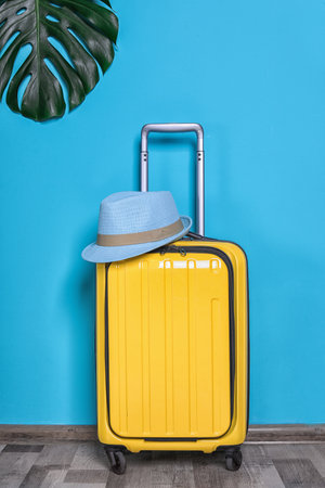 Bright yellow suitcase with hat and tropical leaf near color wall indoorsの写真素材