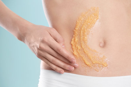 Young woman applying natural scrub on her belly against color background, closeupの写真素材