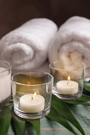Spa composition with burning wax candles, towels and tropical leaf on tableの写真素材
