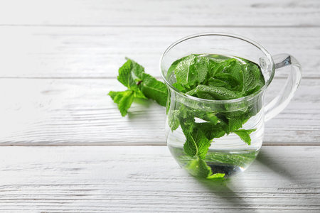 Cup with hot aromatic mint tea on wooden table