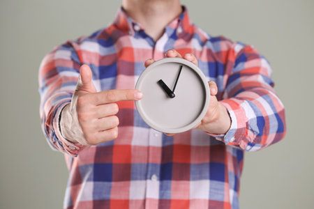 Young man holding alarm clock on gray background. time conceptの写真素材